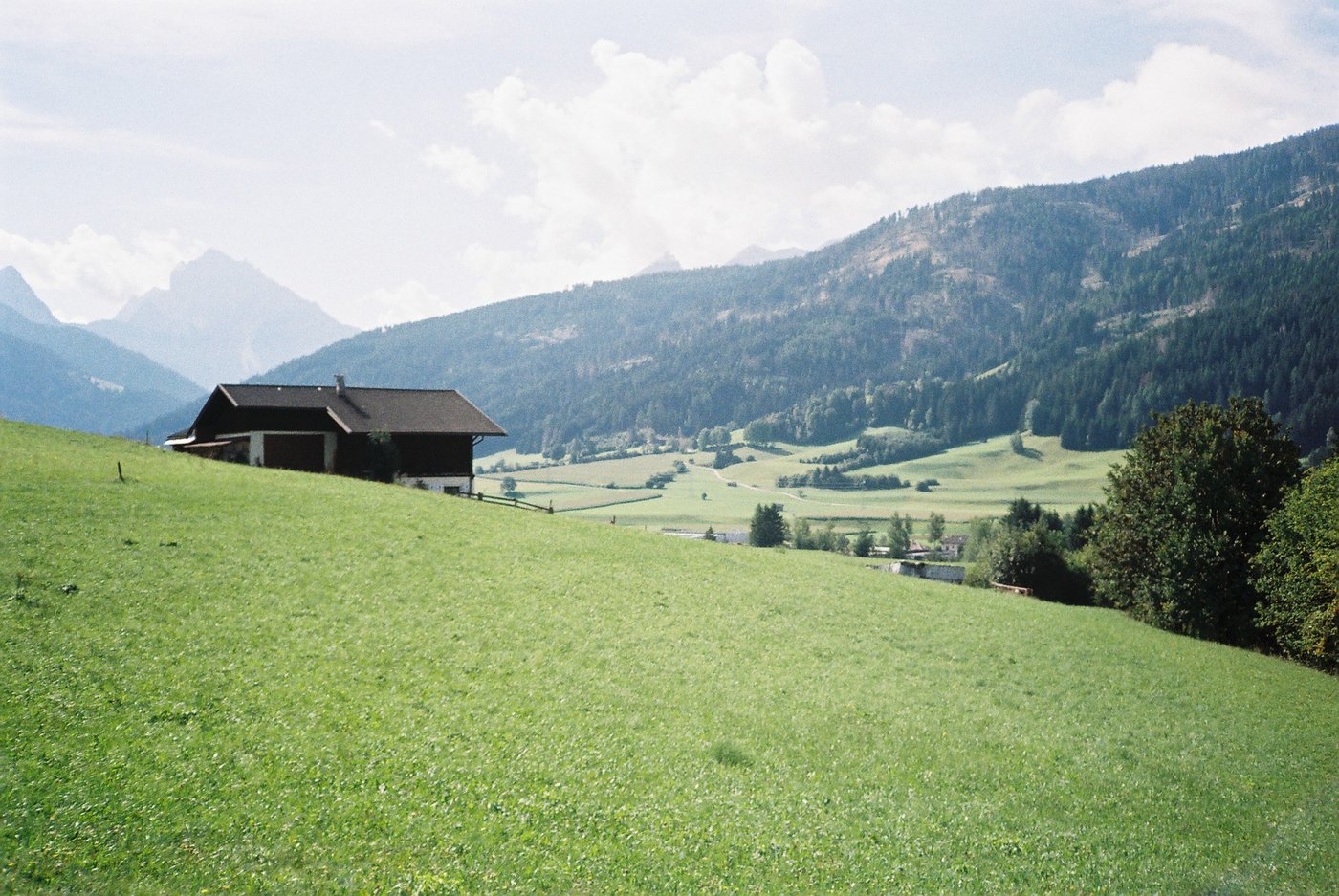 Maso di montagna in mezzo ai prati verdi con le cime delle Dolomiti sullo sfondo, piena luce d'estate. Paesaggio dell'Alto Adige su pellicola a colori 35mm.