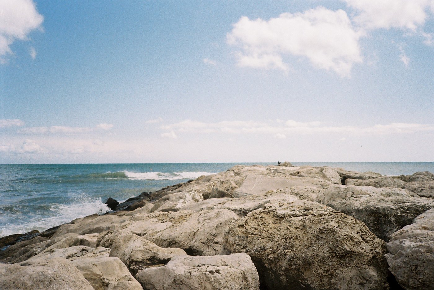 Massi bianchi di una scogliera frangiflutti che si allunga nel mare, cielo azzurro con nuvole. Paesaggio marino su pellicola a colori 35mm.